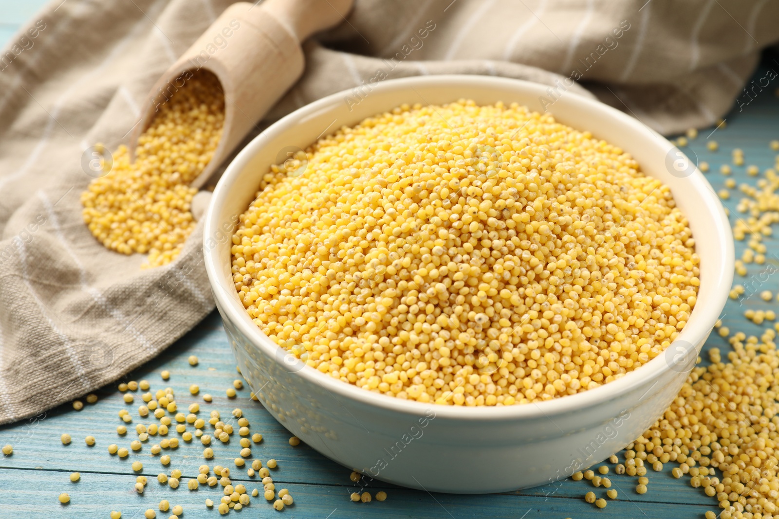 Photo of Millet groats in bowl on light blue wooden table, closeup