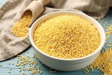Photo of Millet groats in bowl on light blue wooden table, closeup
