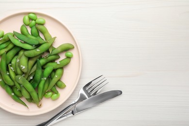 Photo of Green edamame beans in pods served on white wooden table, flat lay. Space for text