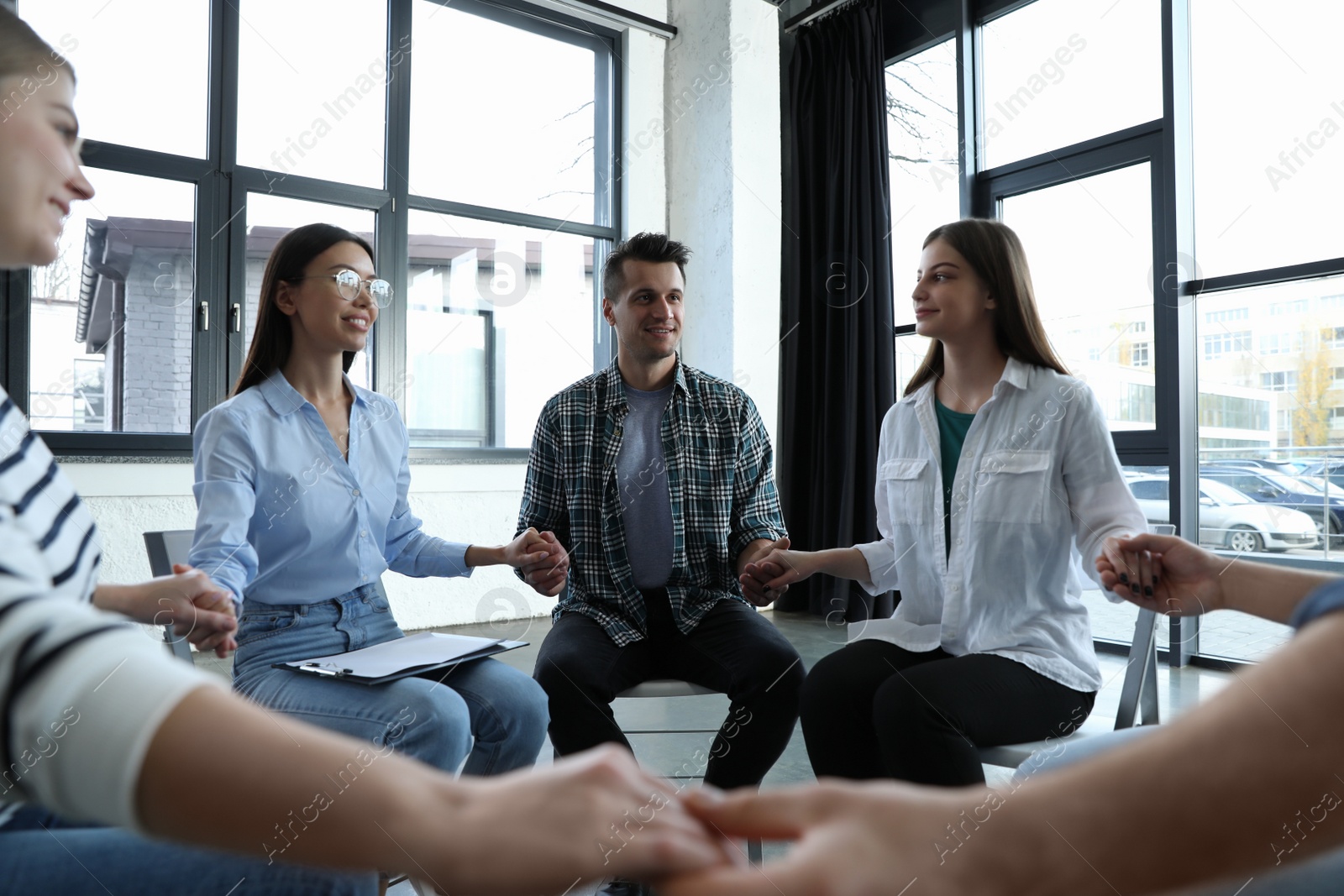 Photo of Psychotherapist holding hands with patients during group therapy session indoors