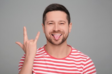Photo of Happy man showing his tongue and rock gesture on grey background