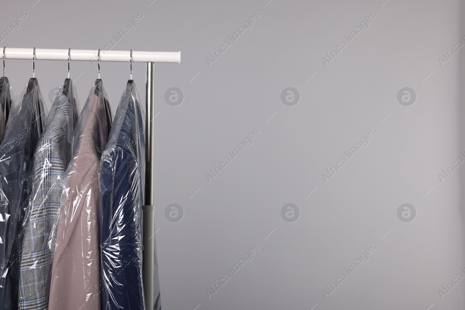 Photo of Dry-cleaning service. Many different clothes in plastic bags hanging on rack against grey background, space for text