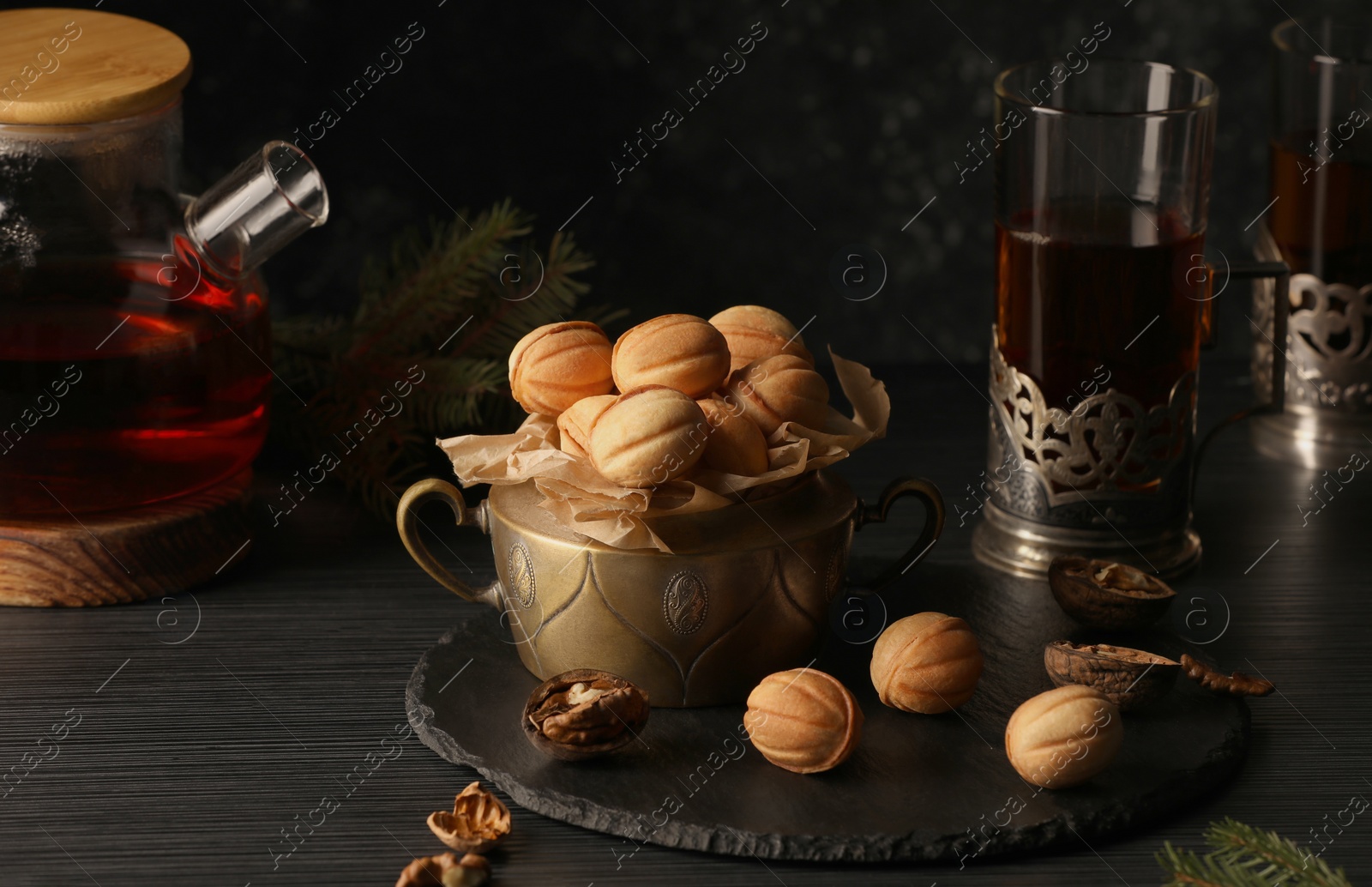 Photo of Aromatic walnut shaped cookies with tasty filling and tea on black table. Homemade pastry carrying nostalgic atmosphere