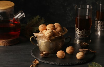 Photo of Aromatic walnut shaped cookies with tasty filling and tea on black table. Homemade pastry carrying nostalgic atmosphere
