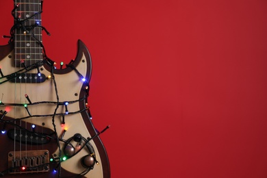 Photo of Closeup view of guitar with fairy lights on red background, space for text. Christmas music