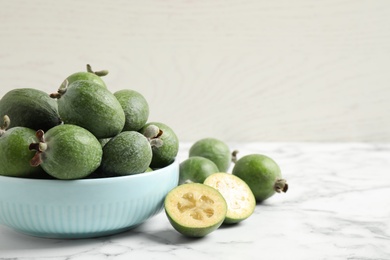 Photo of Fresh green feijoa fruits on white marble table, space for text