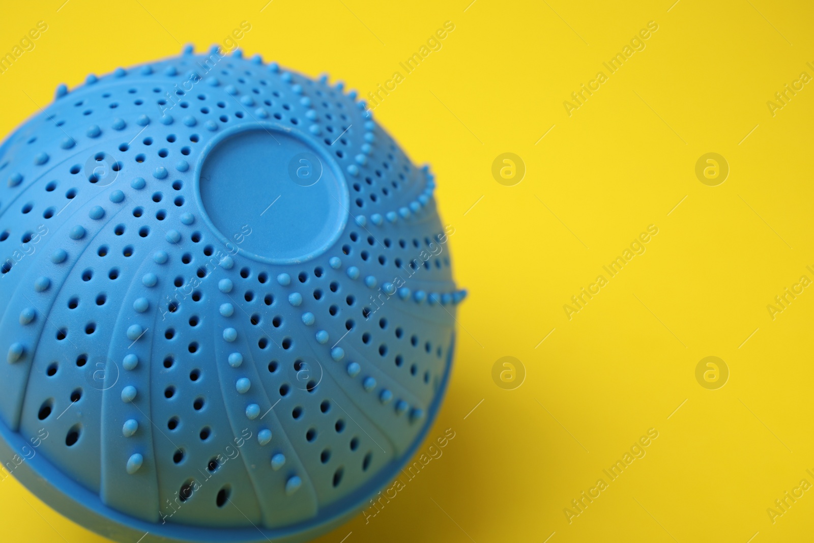 Photo of Laundry dryer ball on yellow background, closeup. Space for text