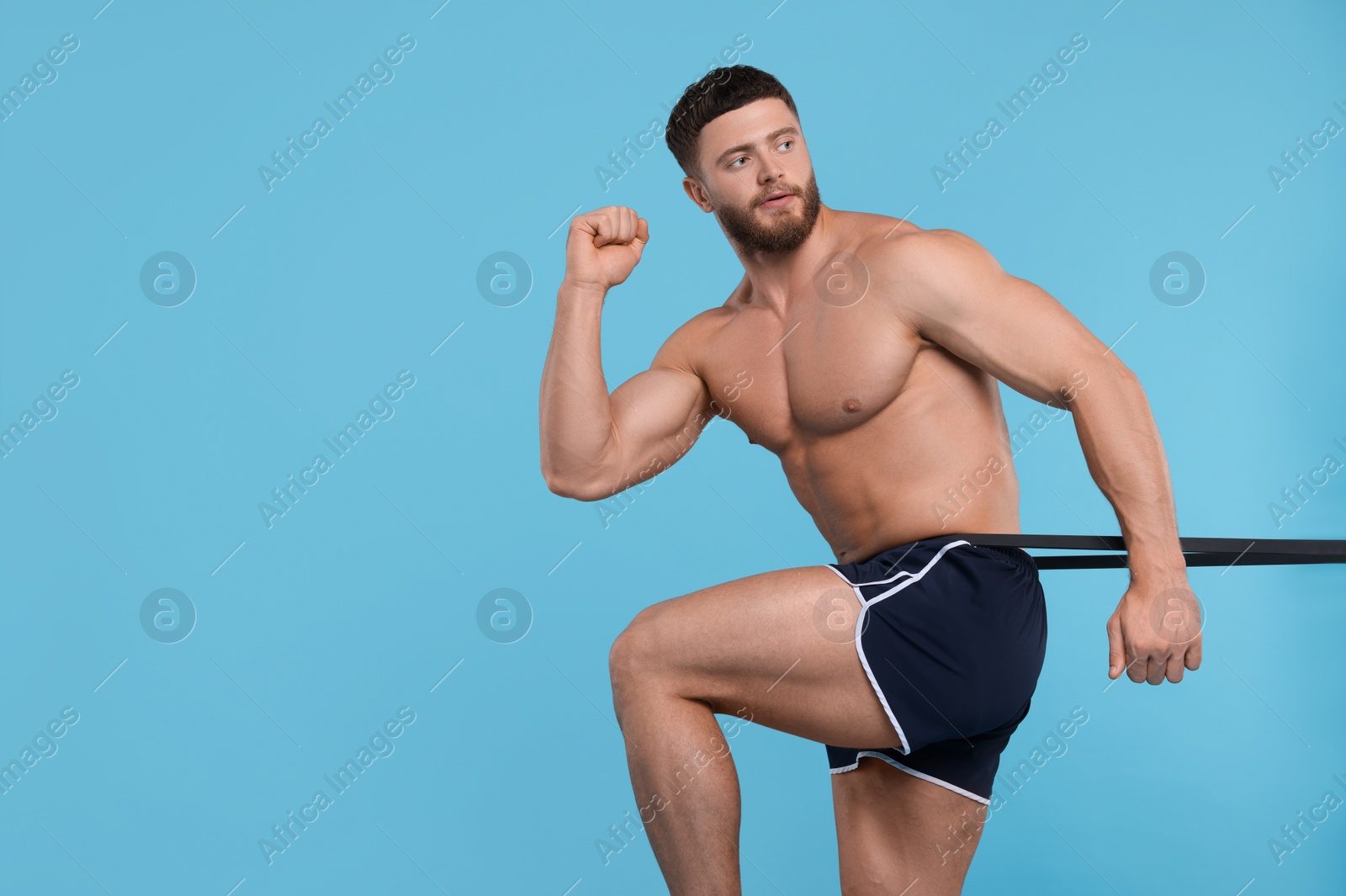 Photo of Young man exercising with elastic resistance band on light blue background. Space for text