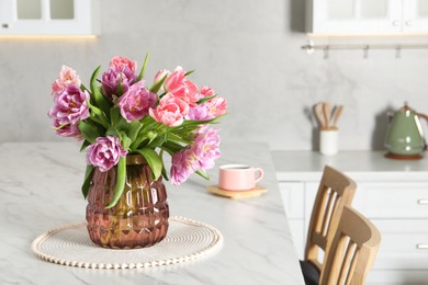 Photo of Beautiful bouquet of colorful tulip flowers on white marble table in kitchen, space for text