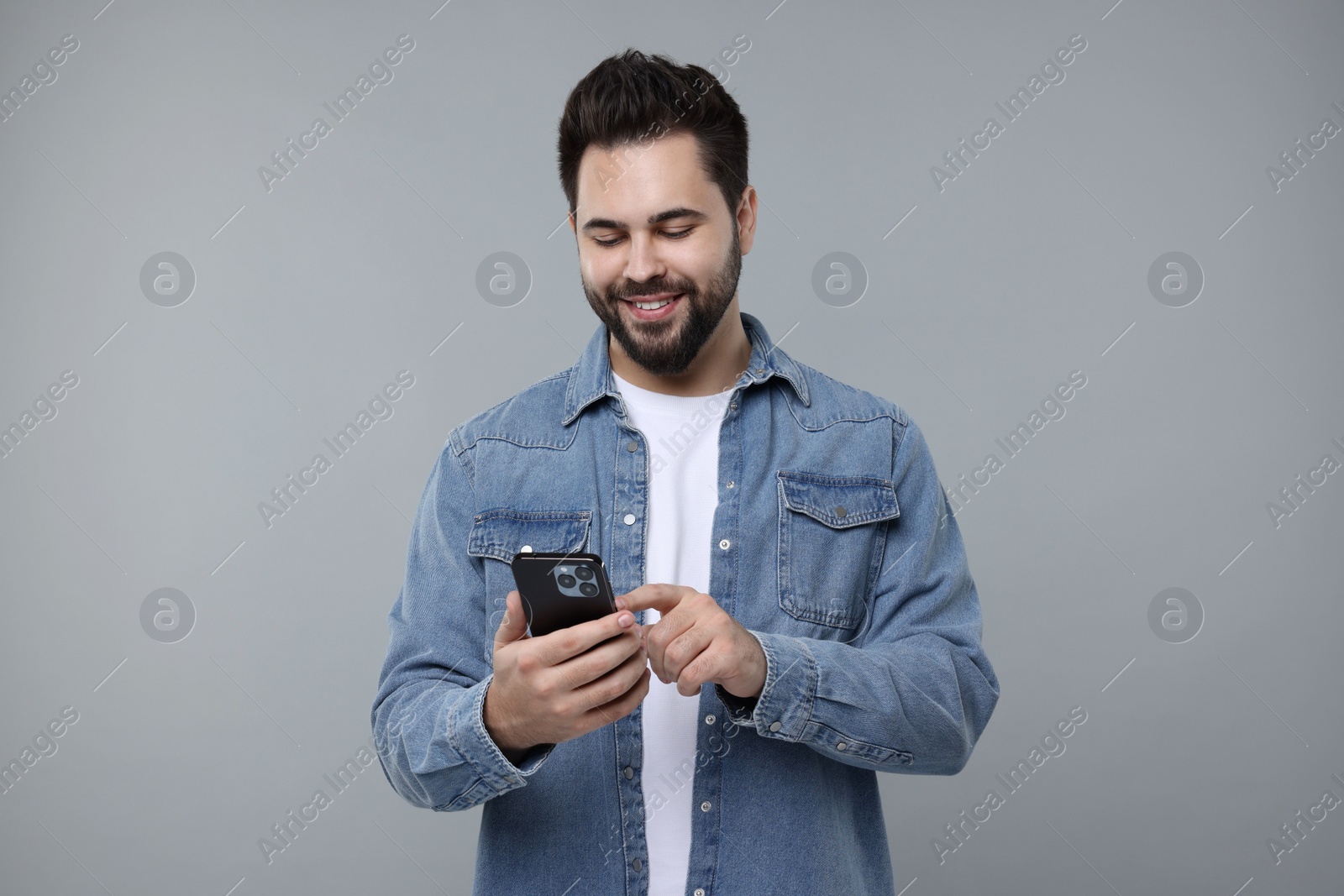 Photo of Happy young man using smartphone on grey background