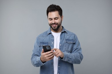 Happy young man using smartphone on grey background