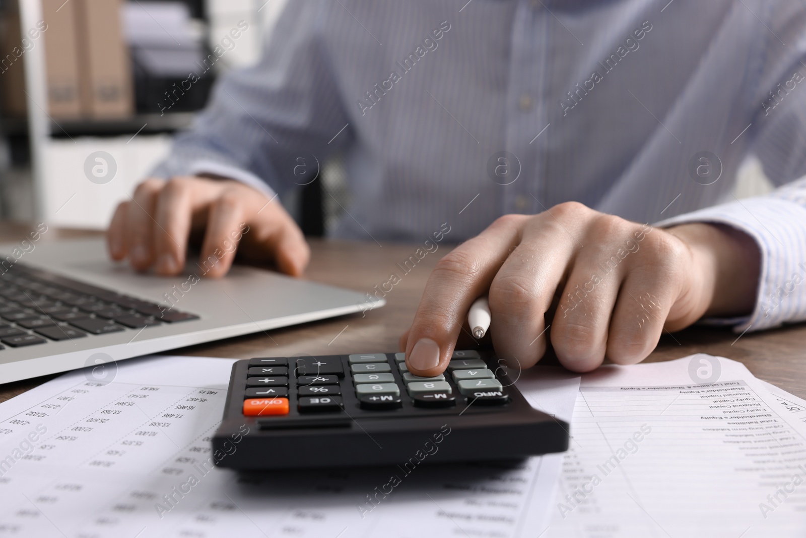 Photo of Man using calculator while working on laptop at table, closeup