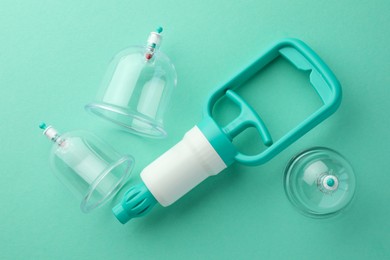 Photo of Plastic cups and hand pump on turquoise background, flat lay. Cupping therapy