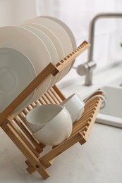 Photo of Drying rack with clean dishes on light marble countertop near sink in kitchen, closeup