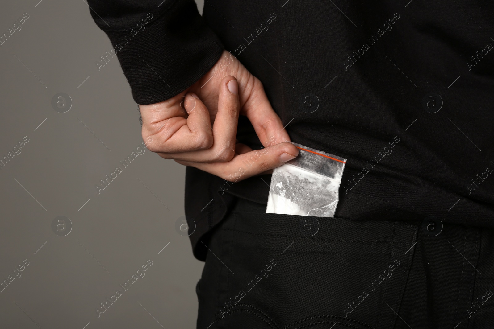 Photo of Drug dealer taking bag with cocaine out of pocket on dark background, closeup. Space for text