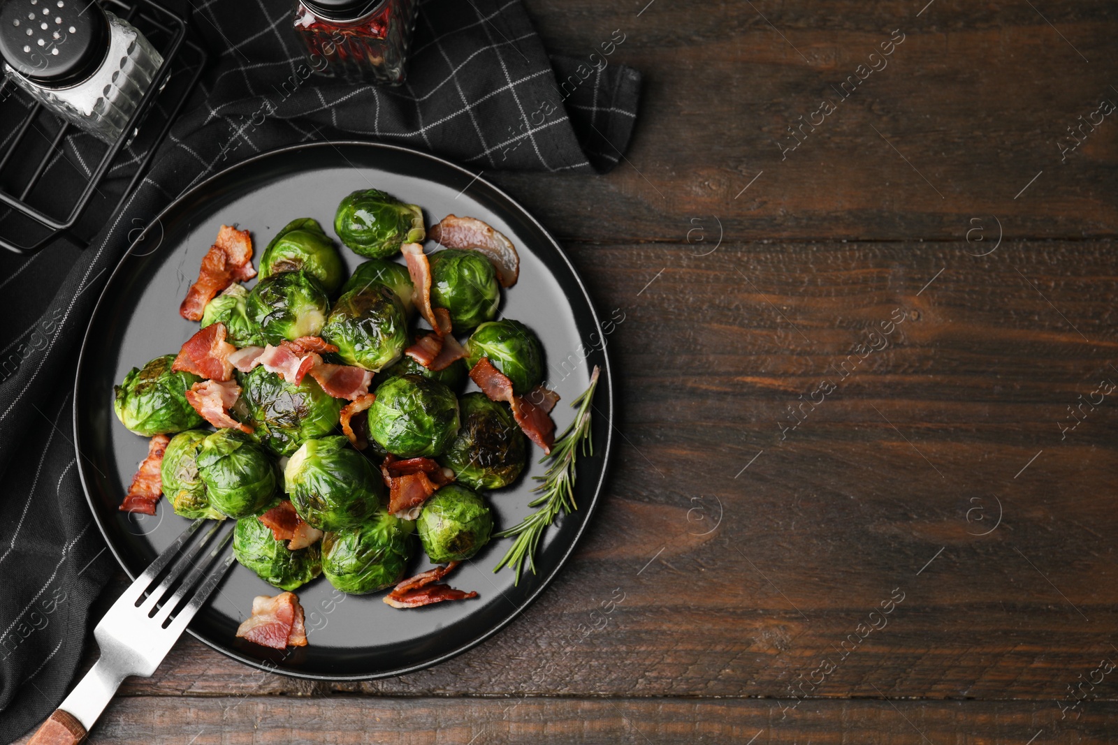 Photo of Delicious roasted Brussels sprouts and bacon on wooden table, top view. Space for text