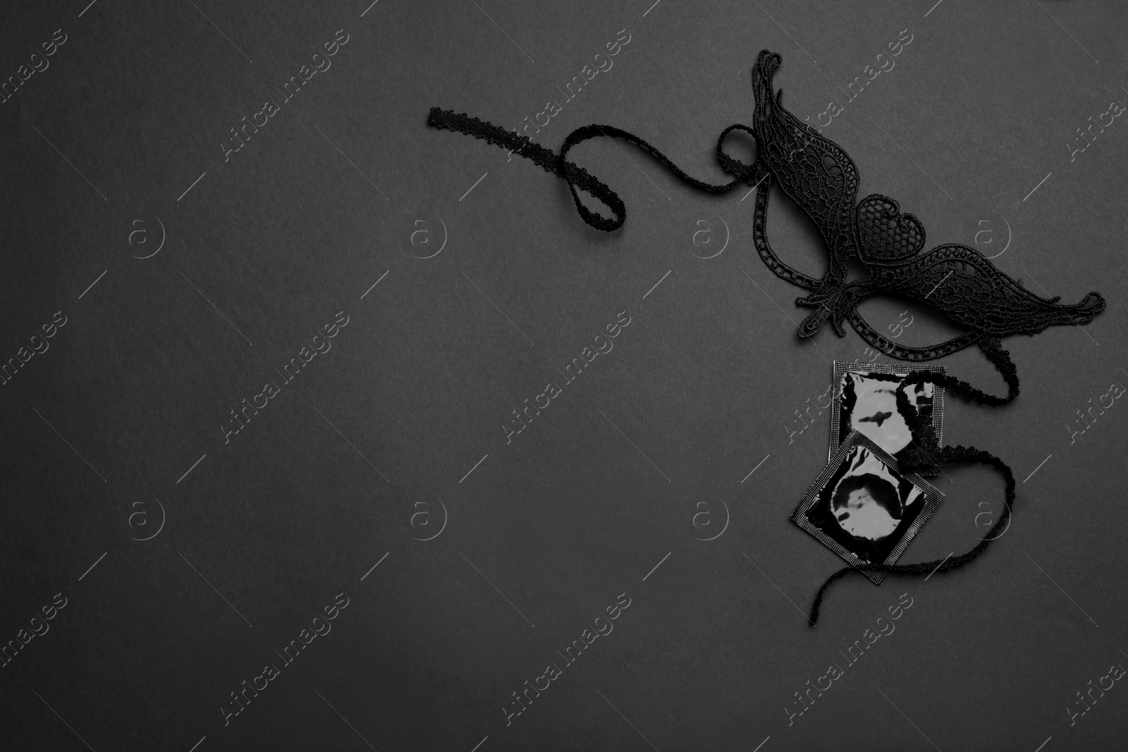 Photo of Lace mask and condoms on black background, top view with space for text. Sex game