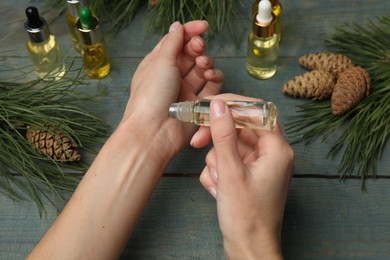 Photo of Woman applying pine essential oil on wrist at light blue wooden table, closeup