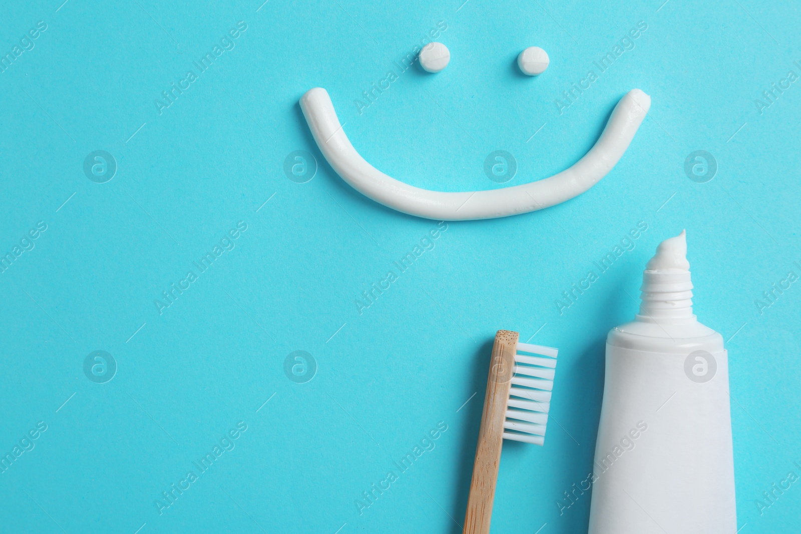 Photo of Smiling face made of toothpaste, tube, brush and space for text on color background, top view