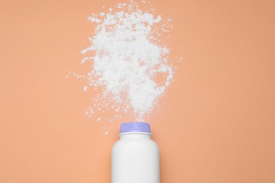 Photo of Bottle and scattered dusting powder on pale coral background, top view. Baby cosmetic product