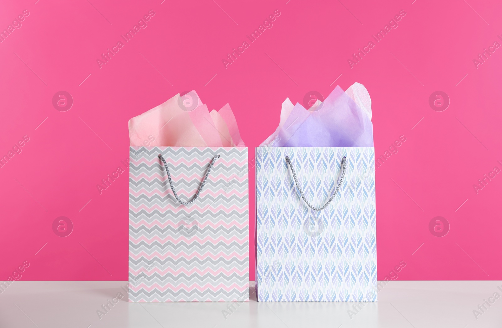 Photo of Gift bags with paper on white table against pink background