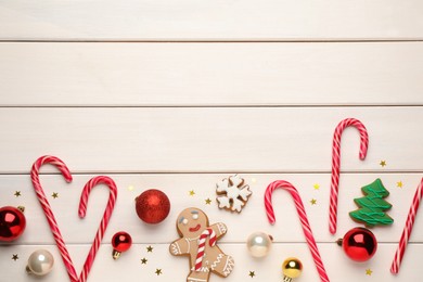 Photo of Tasty candy canes, gingerbread cookies and Christmas balls on white wooden table, flat lay. Space for text