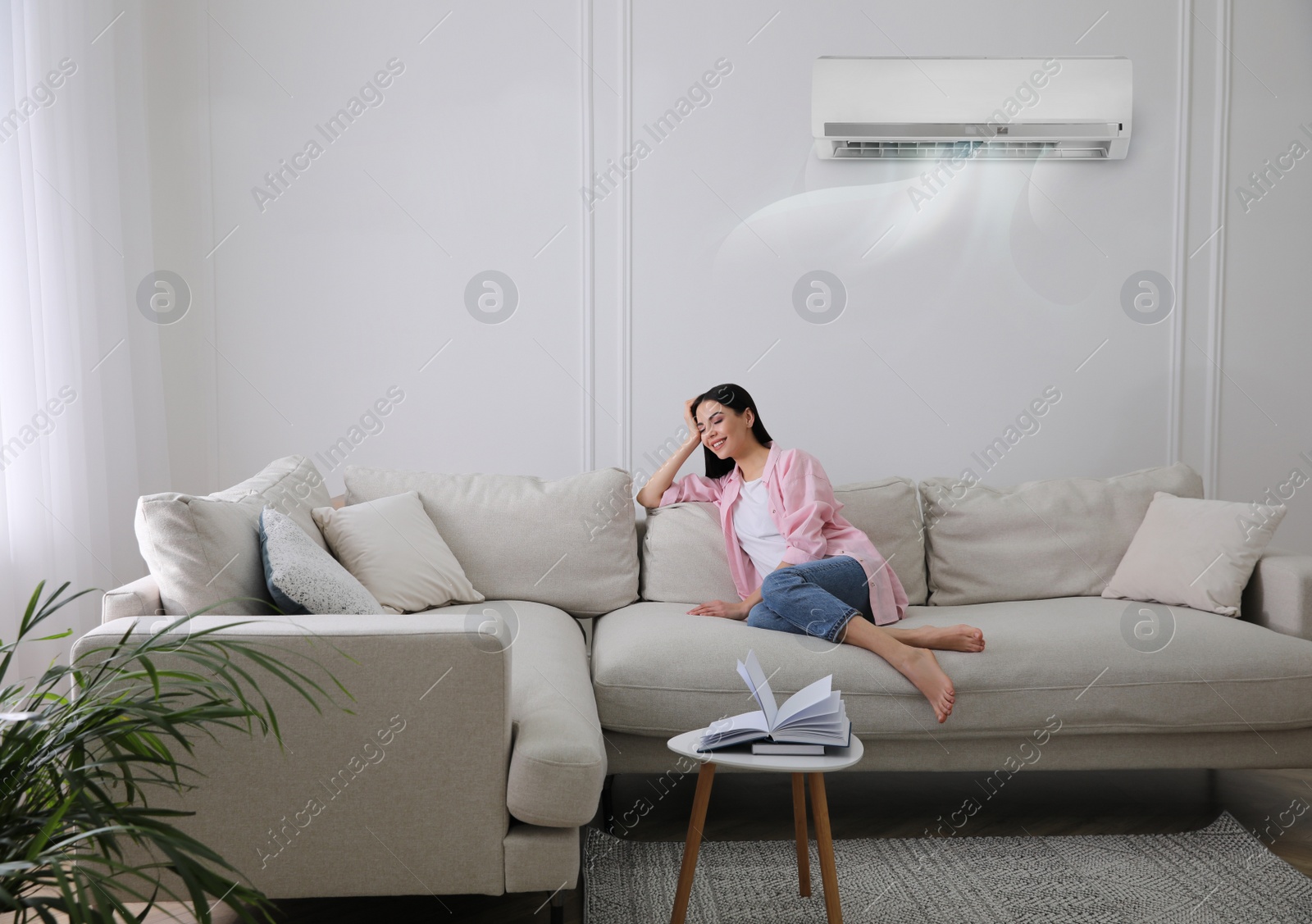 Image of Young woman resting under air conditioner on white wall at home