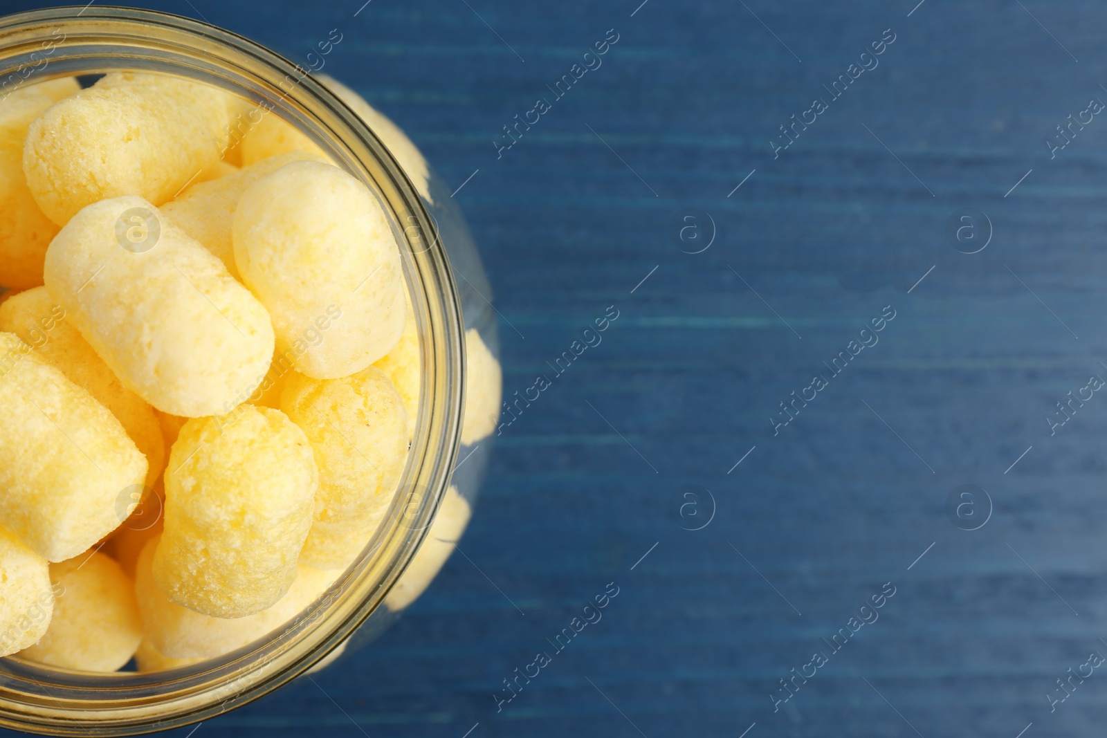 Photo of Jar of delicious crispy corn sticks on blue wooden table, top view. Space for text