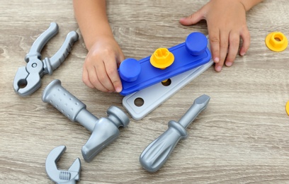 Photo of Little boy playing with toy construction tools at wooden table, closeup