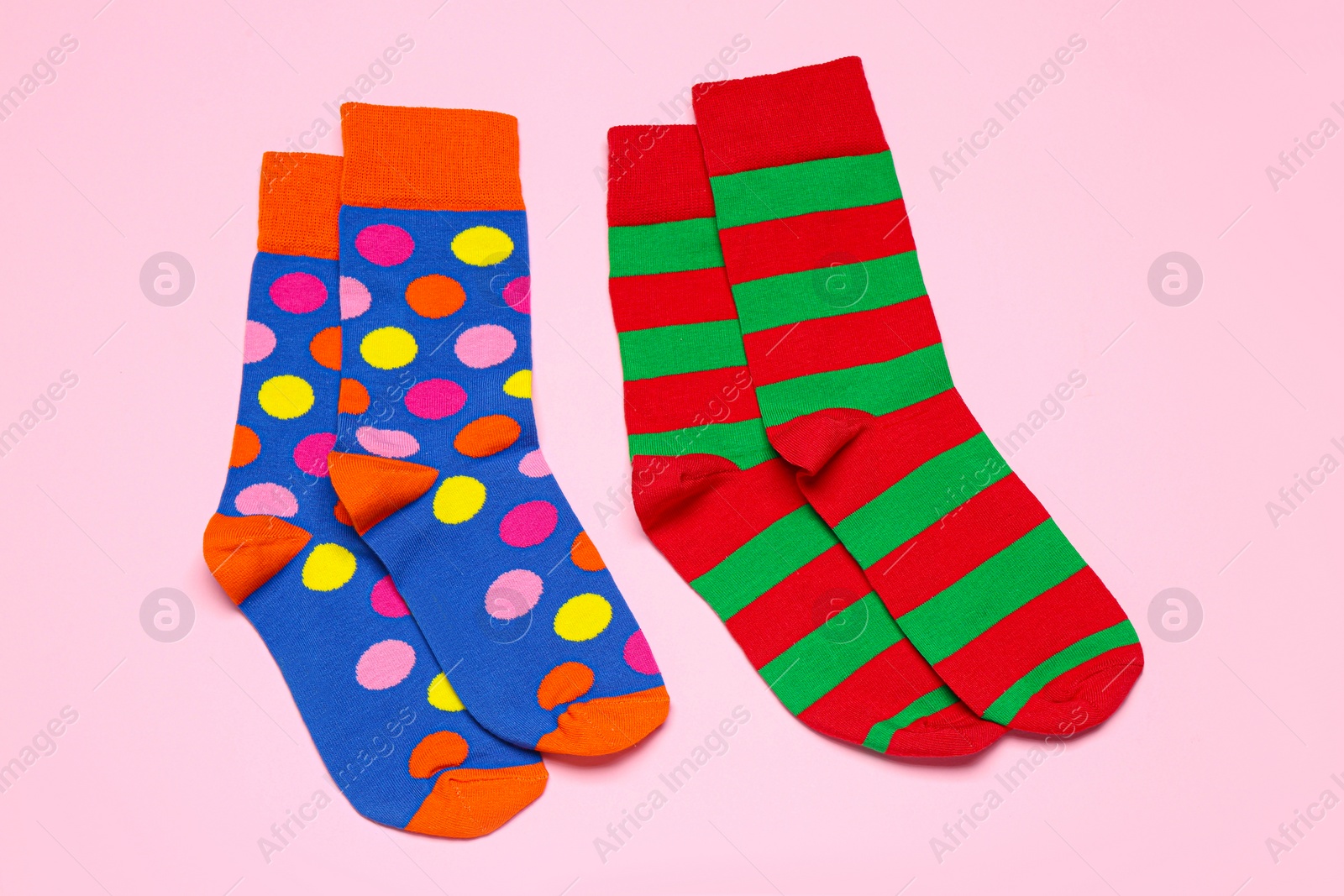 Photo of Different colorful socks on light pink background, flat lay