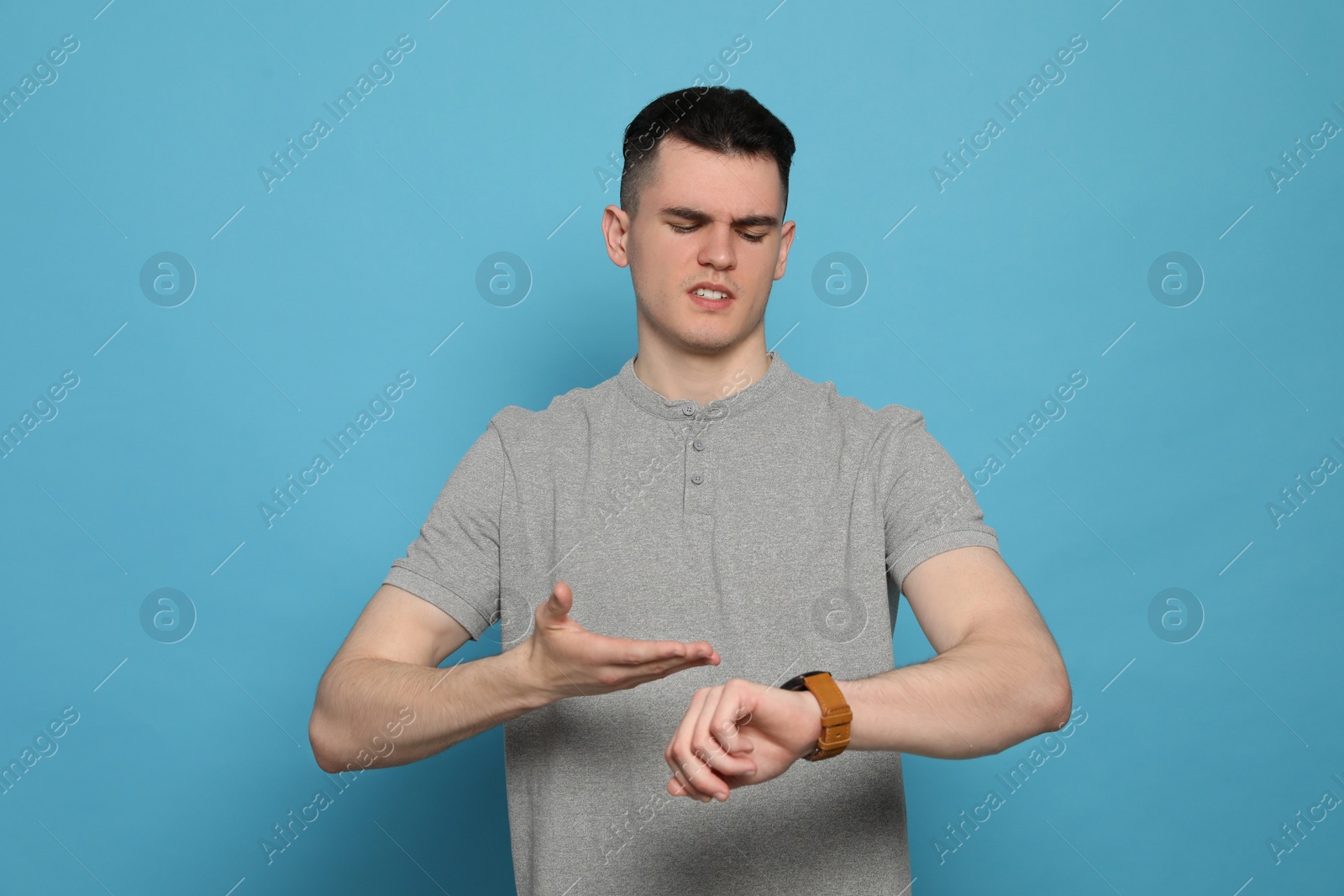 Photo of Emotional young man checking time on light blue background. Being late concept