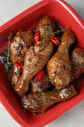 Chicken legs glazed in soy sauce with black sesame, chili pepper and thyme on light table, top view