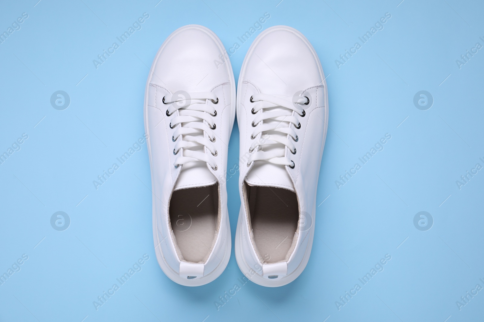 Photo of Pair of stylish white sneakers on light blue background, top view