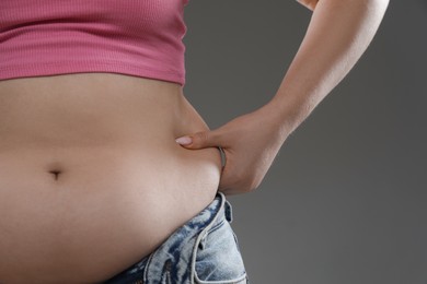Woman touching belly fat on grey background, closeup. Overweight problem