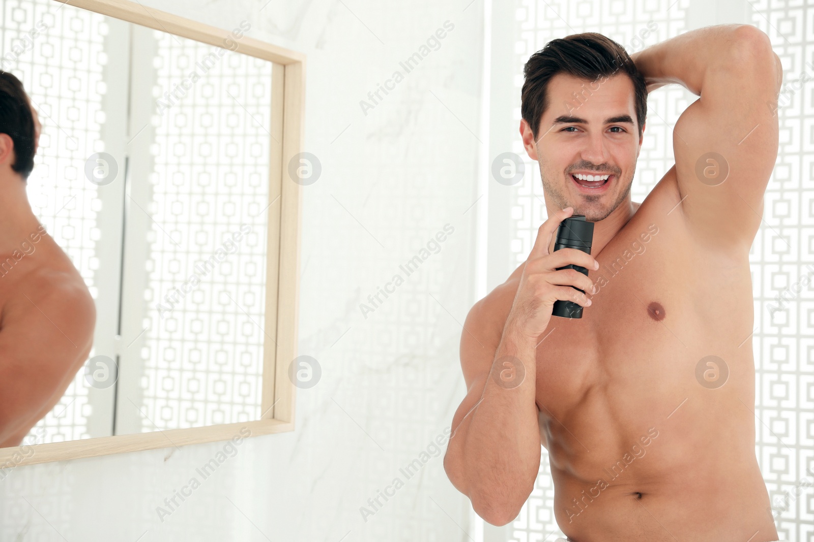 Photo of Handsome young man applying deodorant in bathroom