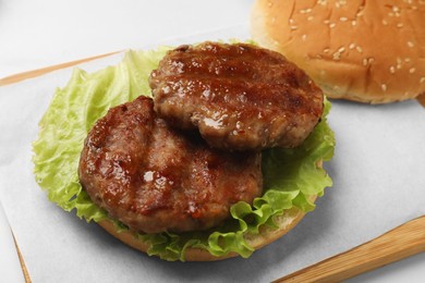 Photo of Delicious fried patties, lettuce and bun on white table, closeup. Making hamburger