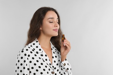 Photo of Beautiful young woman with bottle of essential oil on light grey background, space for text