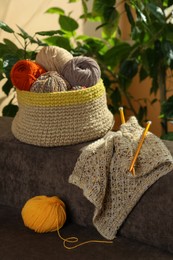 Photo of Soft woolen yarns, knitting and needles on brown sofa indoors