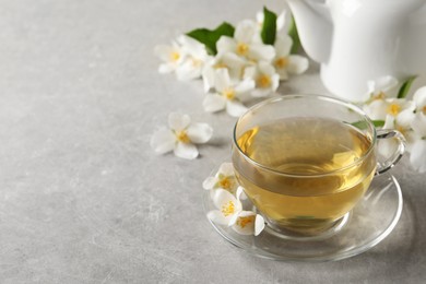Photo of Glass cup of jasmine tea and fresh flowers on grey table. Space for text