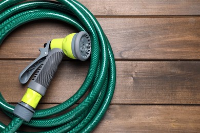 Photo of Green garden hose with spray gun on wooden table, top view. Space for text