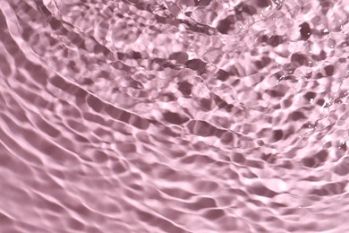 Rippled surface of clear water on pink background, top view