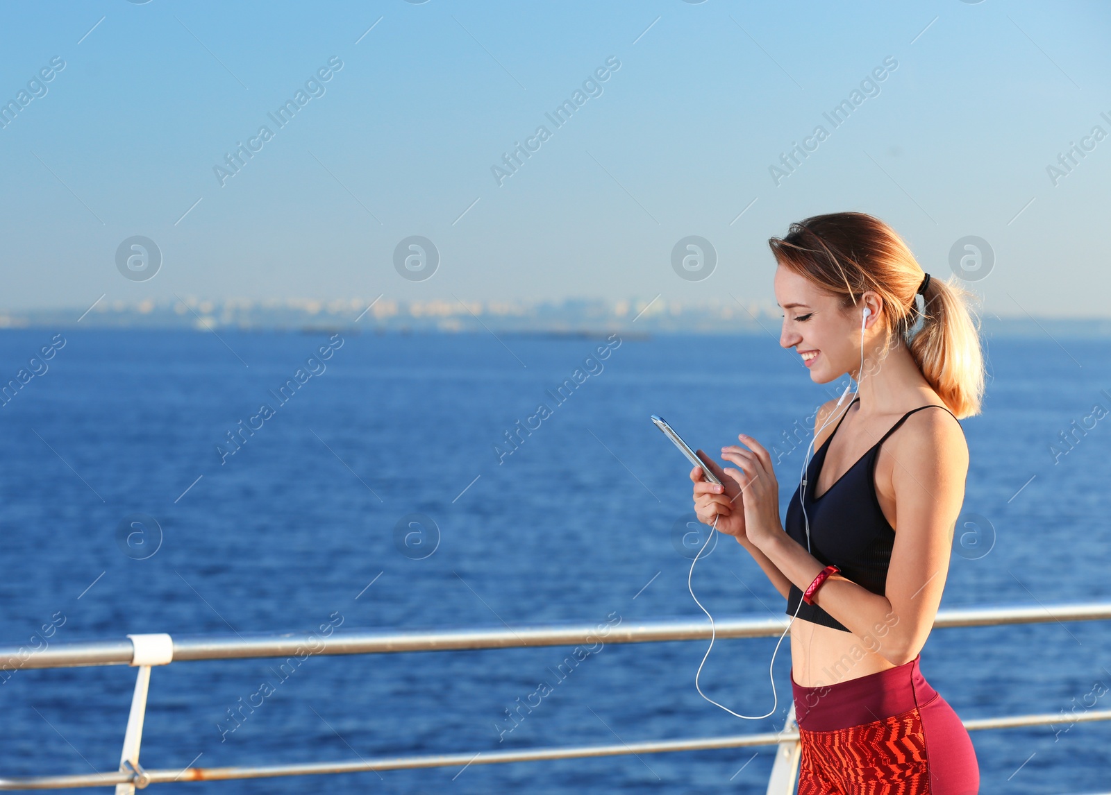 Photo of Young woman choosing music for fitness exercises on pier in morning