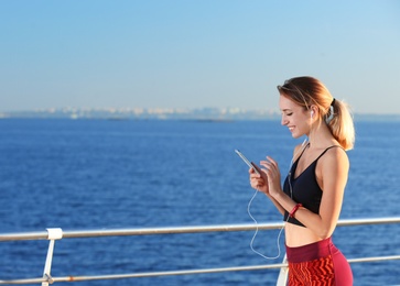 Young woman choosing music for fitness exercises on pier in morning