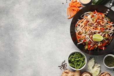 Photo of Shrimp stir fry with noodles and vegetables in wok surrounded by ingredients on grey table, flat lay. Space for text