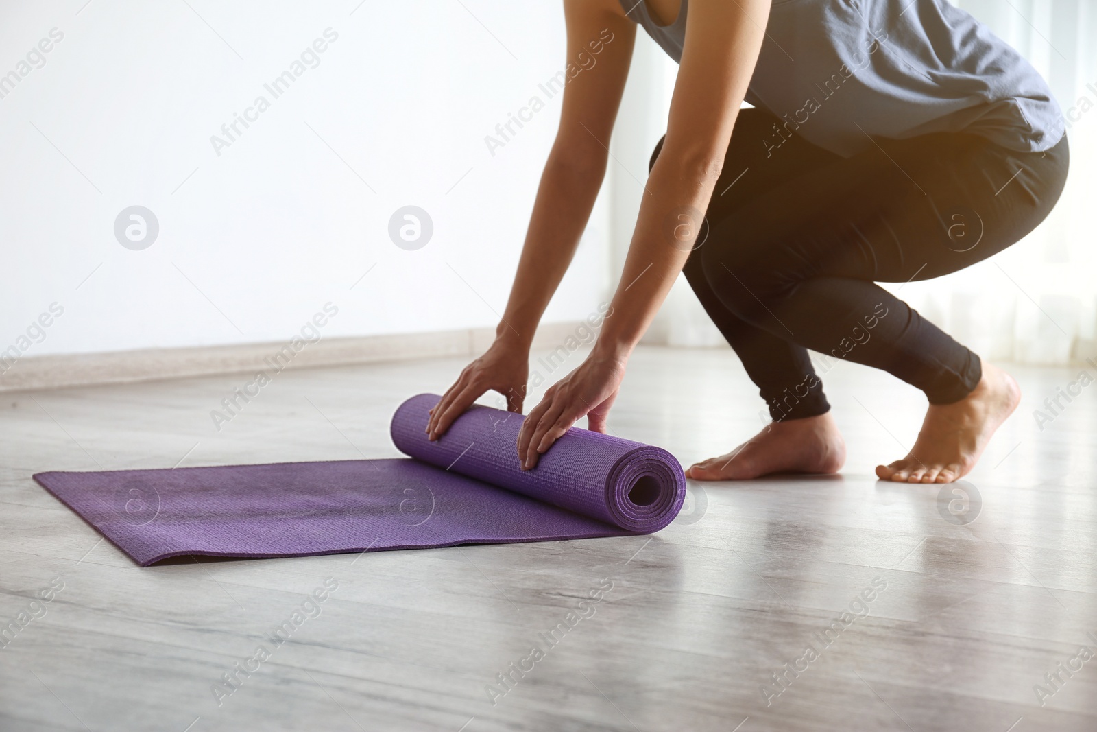 Photo of Woman rolling yoga mat on floor indoors, closeup