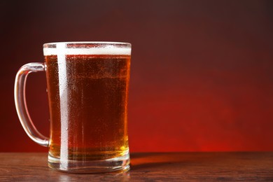Mug with fresh beer on wooden table against color background. Space for text