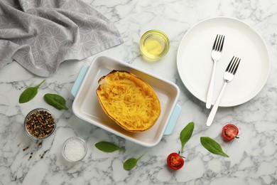 Photo of Half of cooked spaghetti squash in baking dish, plate and ingredients on white marble table, flat lay