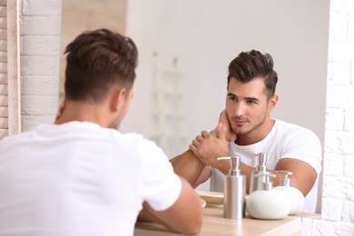 Photo of Young man with stubble ready for shaving near mirror in bathroom