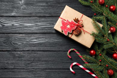 Gift box, candy canes, fir tree branches and Christmas decor on black wooden table, flat lay. Space for text