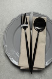 Stylish cutlery, napkin and plate on grey table, top view